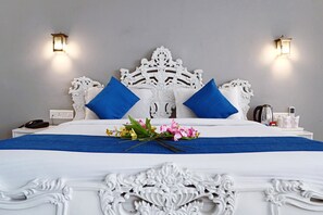 Una cama bien hecha con cabecera blanca, almohadas azules y colcha azul. Hay dos lámparas fijadas a la pared a cada lado de la cama.