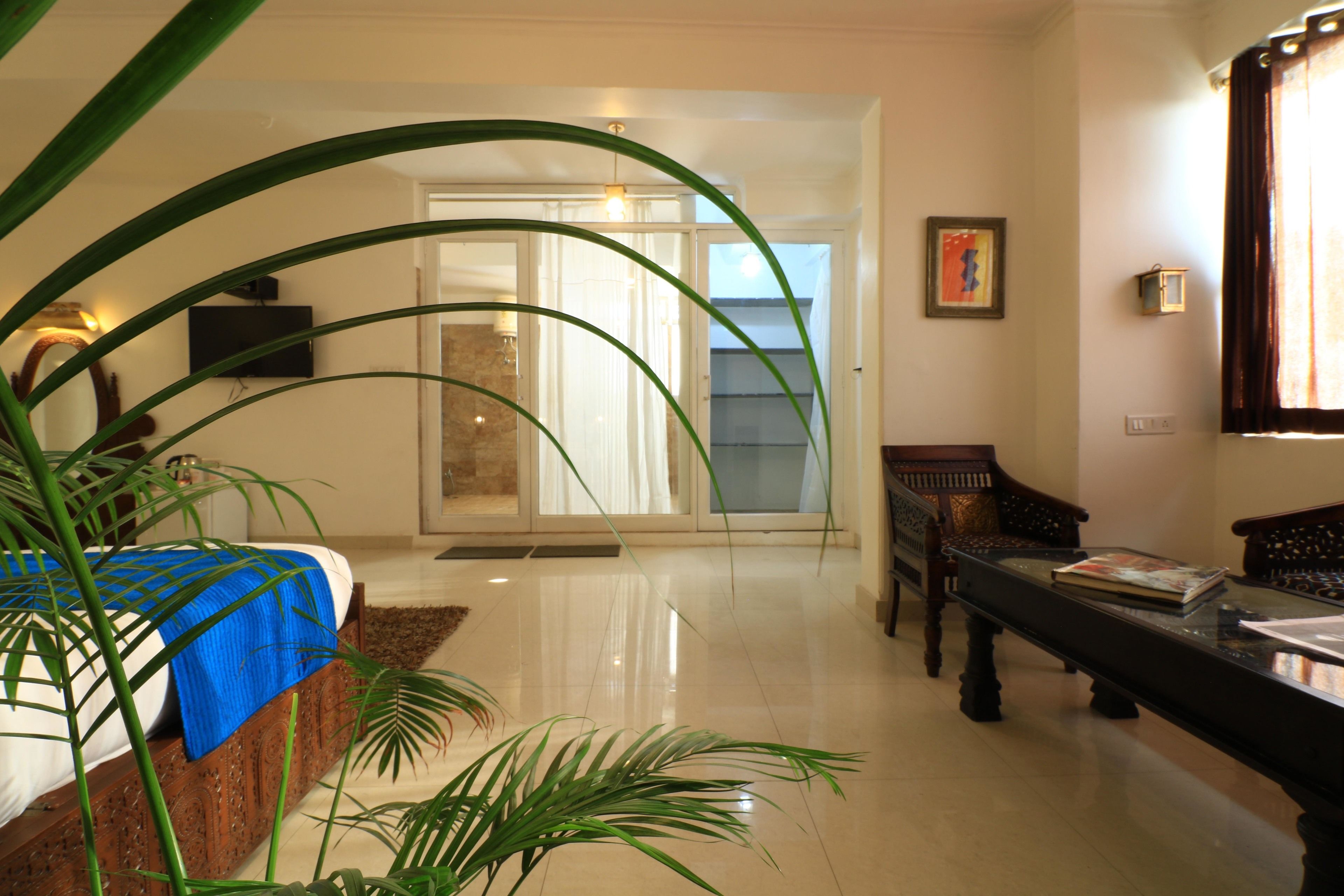 Une chambre d’hôtel avec un lit, un banc en bois, une table et une grande fenêtre avec des rideaux.