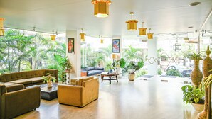 A spacious lobby with a modern design, featuring a large sofa, a coffee table, and several potted plants. - Hotel Dodas Palace (Jaipur)