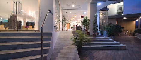 A modern hotel lobby with a wooden staircase, potted plants, and a glass entrance.