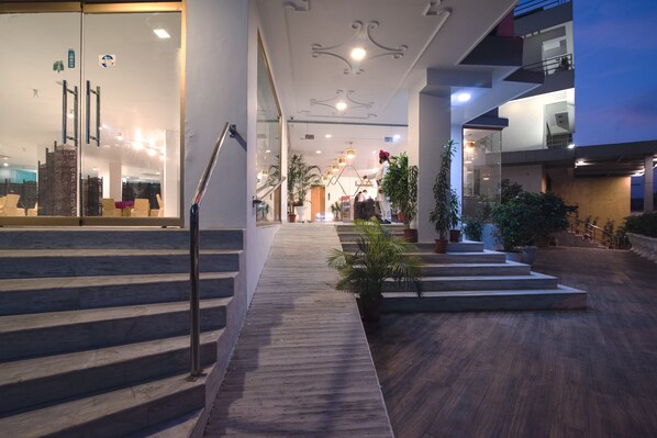 A modern hotel lobby with a wooden staircase, potted plants, and a glass entrance.