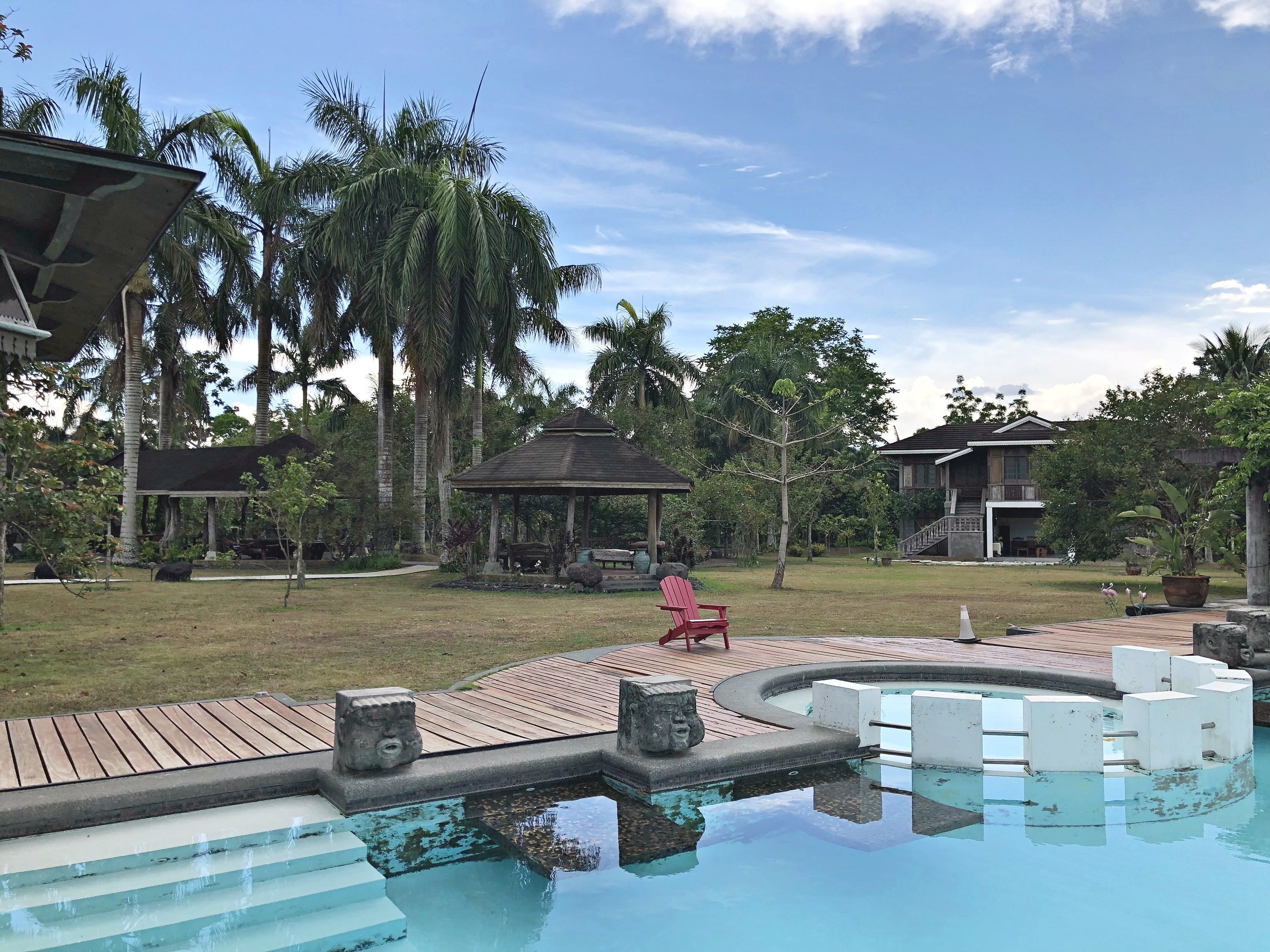 Un área de piscina con un pabellón, palmeras y una terraza de madera.