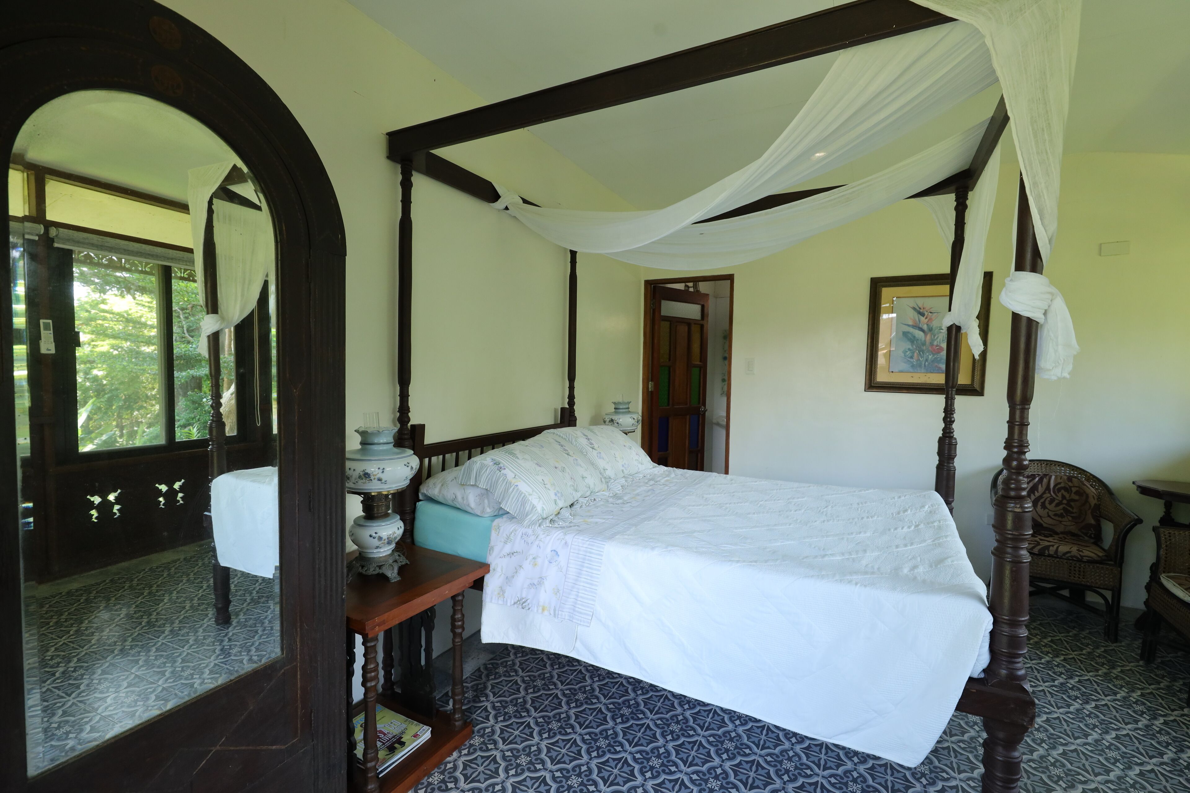 A four-poster bed with a canopy, a wooden nightstand, a chair, and a patterned floor.