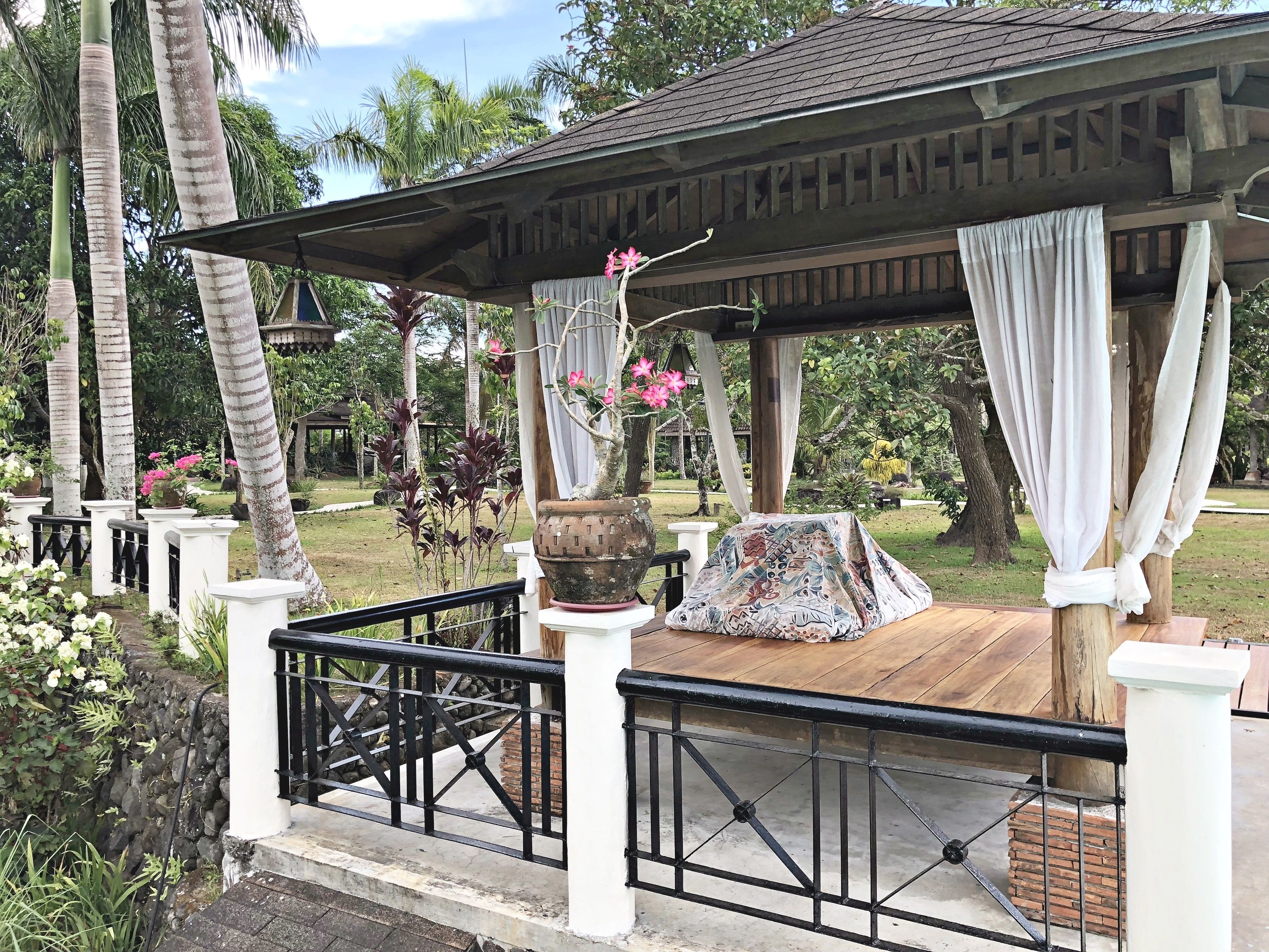 A covered outdoor seating area with a wooden deck, white columns, and a black railing.