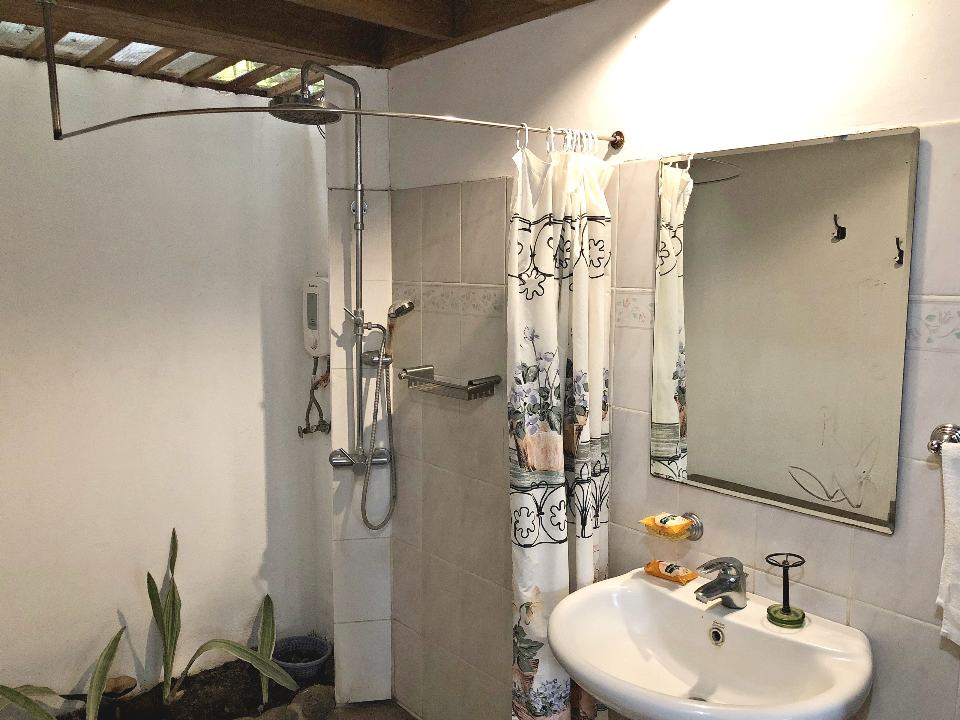 Une salle de bain équipée d’une douche, d’un lavabo, d’un miroir et d’un rideau orné de motifs floraux.