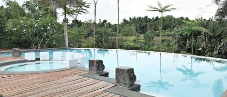 Una piscina con cubierta de madera y pilares de piedra, rodeada de exuberante vegetación y palmeras.