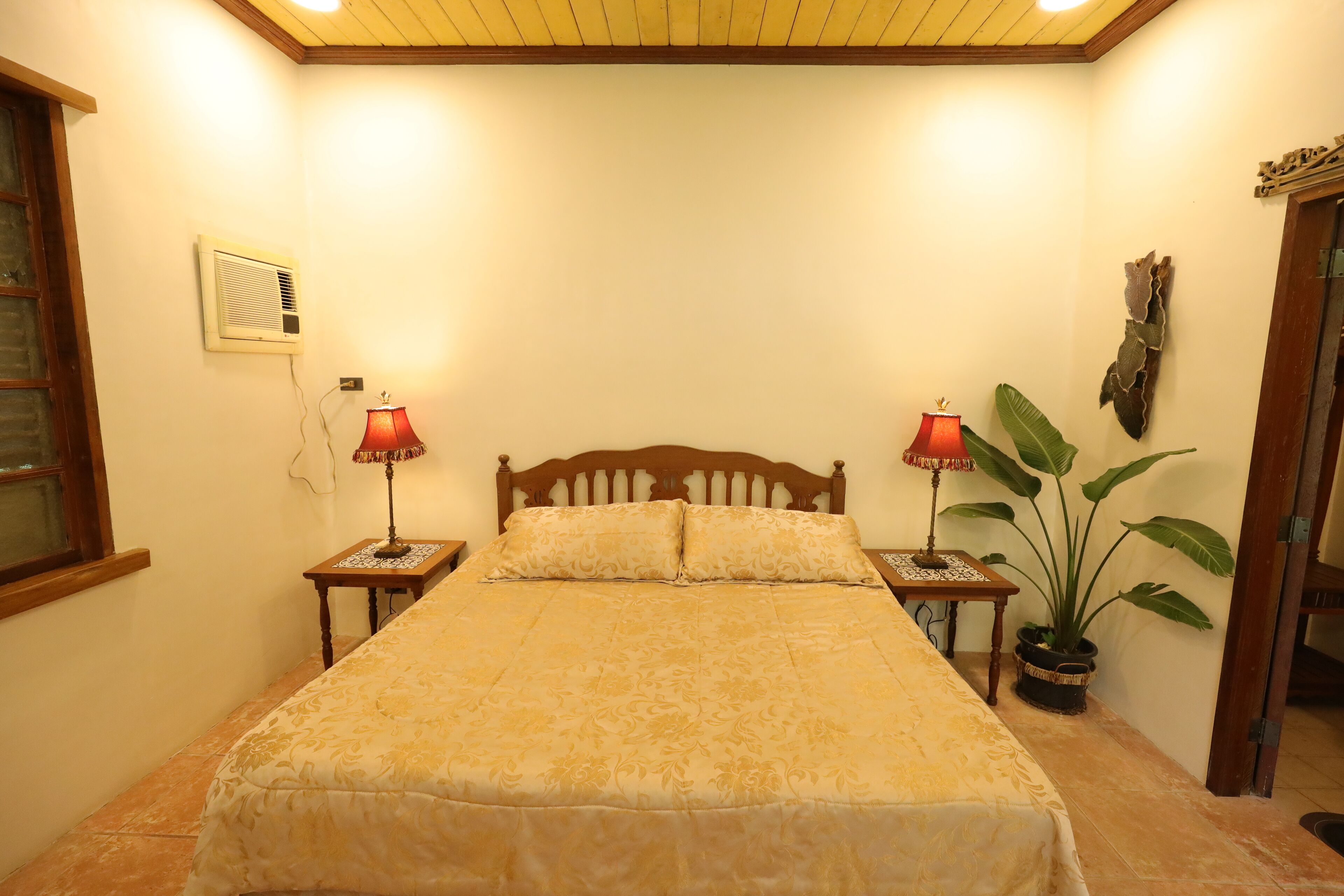 Un dormitorio con una cama grande, dos mesitas de noche con lámparas, una planta en maceta y un cabecero de madera.