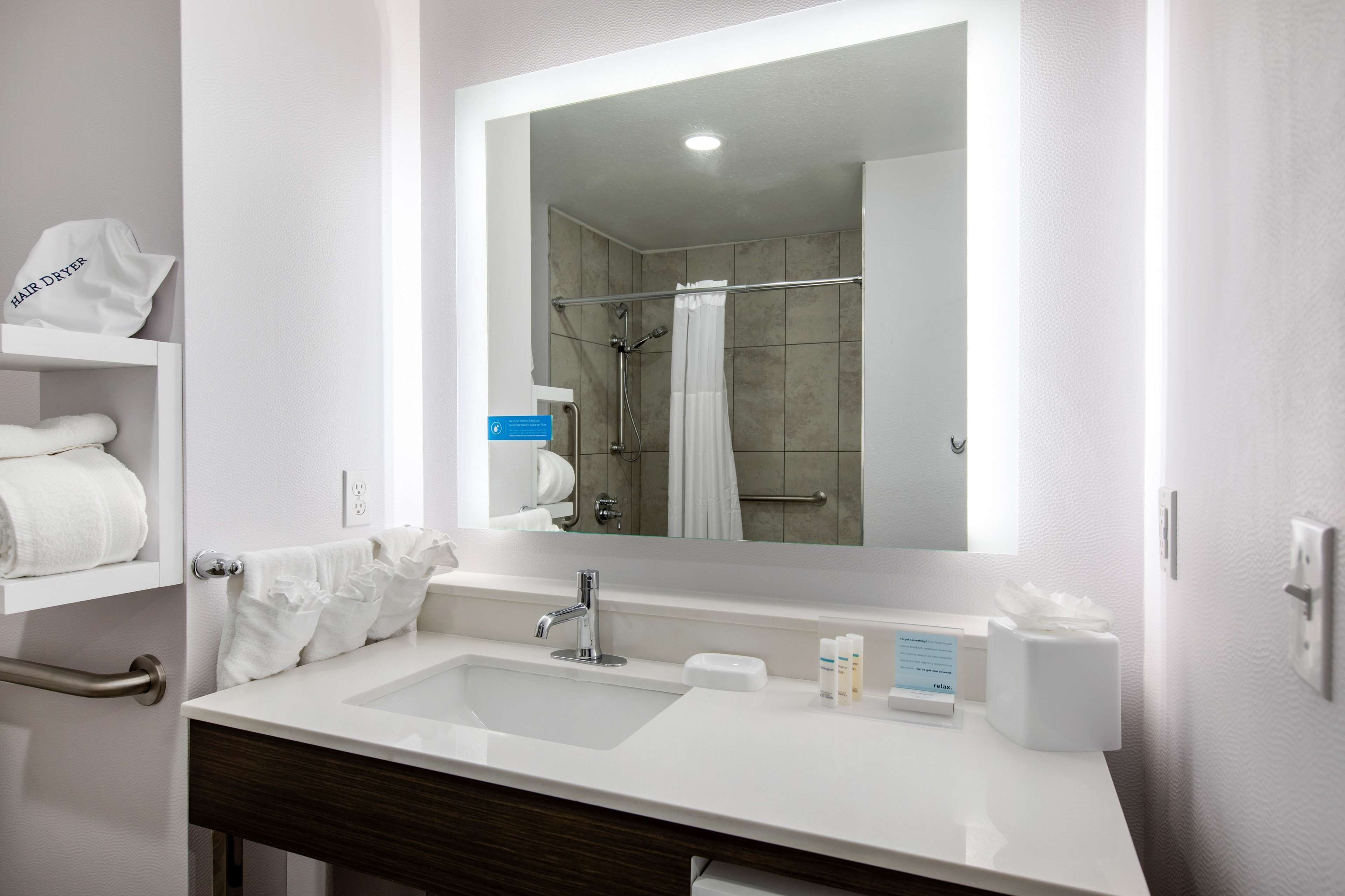 Un baño moderno con un lavamanos blanco, un espejo, toallero y zona de ducha.