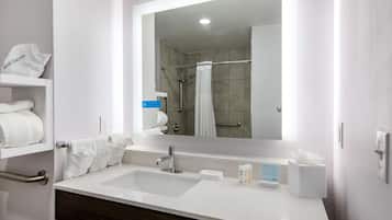 Un baño moderno con un lavamanos blanco, un espejo, toallero y zona de ducha.