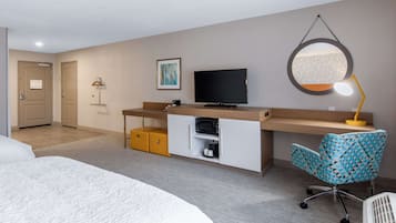 A hotel room with a bed, a desk with a TV, a desk lamp, and a chair.
