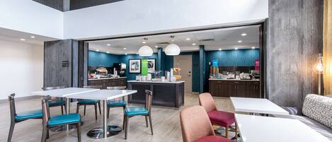 A modern hotel lobby with a dining area, a kitchen, and a seating area.