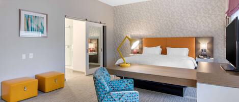 Et moderne hotelværelse med seng, skrivebord, stol og fjernsyn.