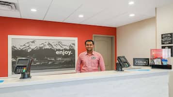 A hotel reception desk with a red wall, a framed picture of mountains, and a sign that says "enjoy."