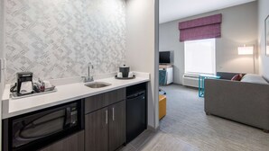 A modern kitchen with a microwave, coffee maker, and dishwasher. There is a window with a purple valance and a sofa in the living area. - Hampton Inn & Suites Ruidoso Downs (Ruidoso Downs)