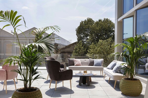 An outdoor seating area with modern furniture, potted plants, and a view of a building.