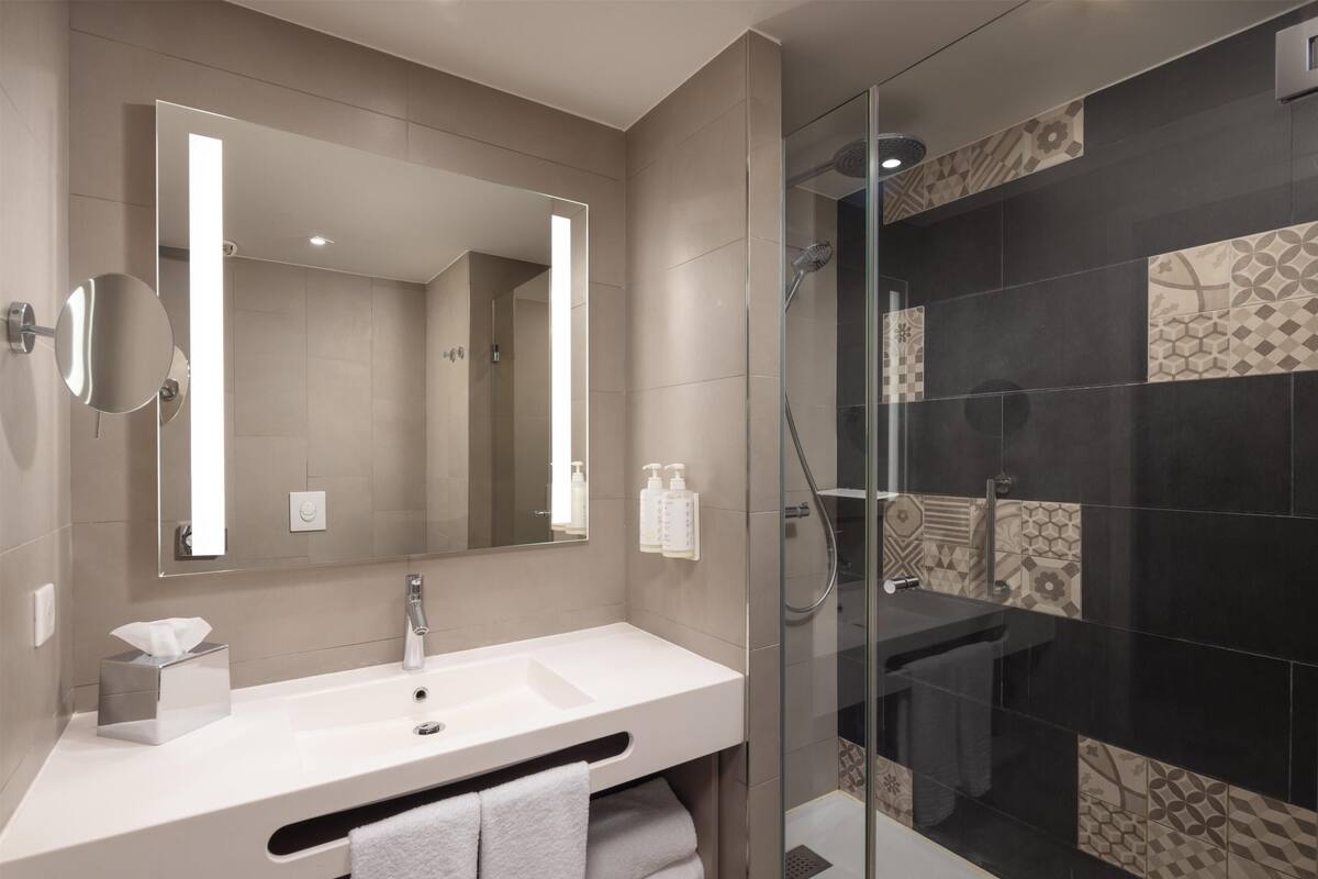 A modern bathroom with a large mirror, a white sink, and a glass-enclosed shower area.