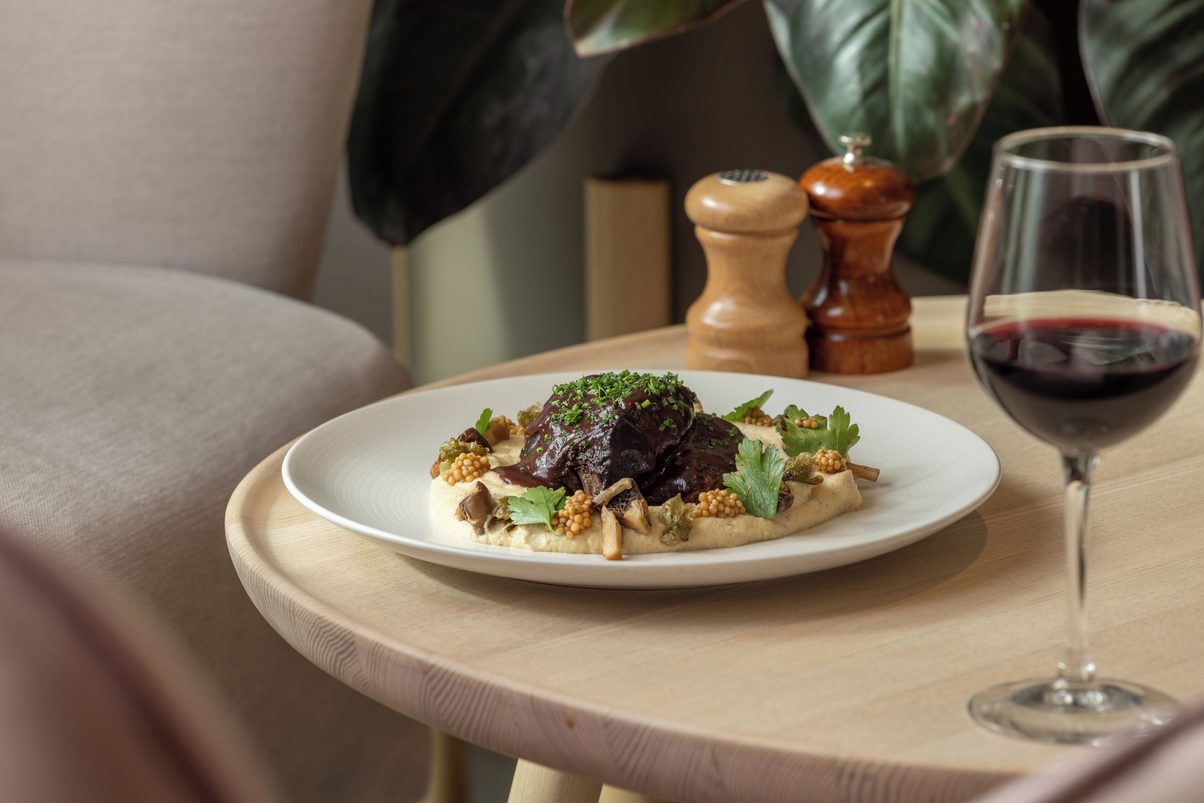 Un plato de comida sobre una mesa de madera con una copa de vino tinto.