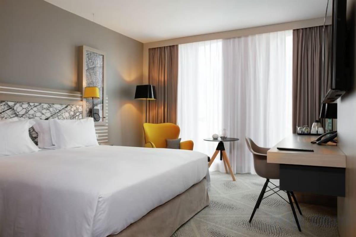 A hotel room with a large bed, a desk, a chair, and a television.