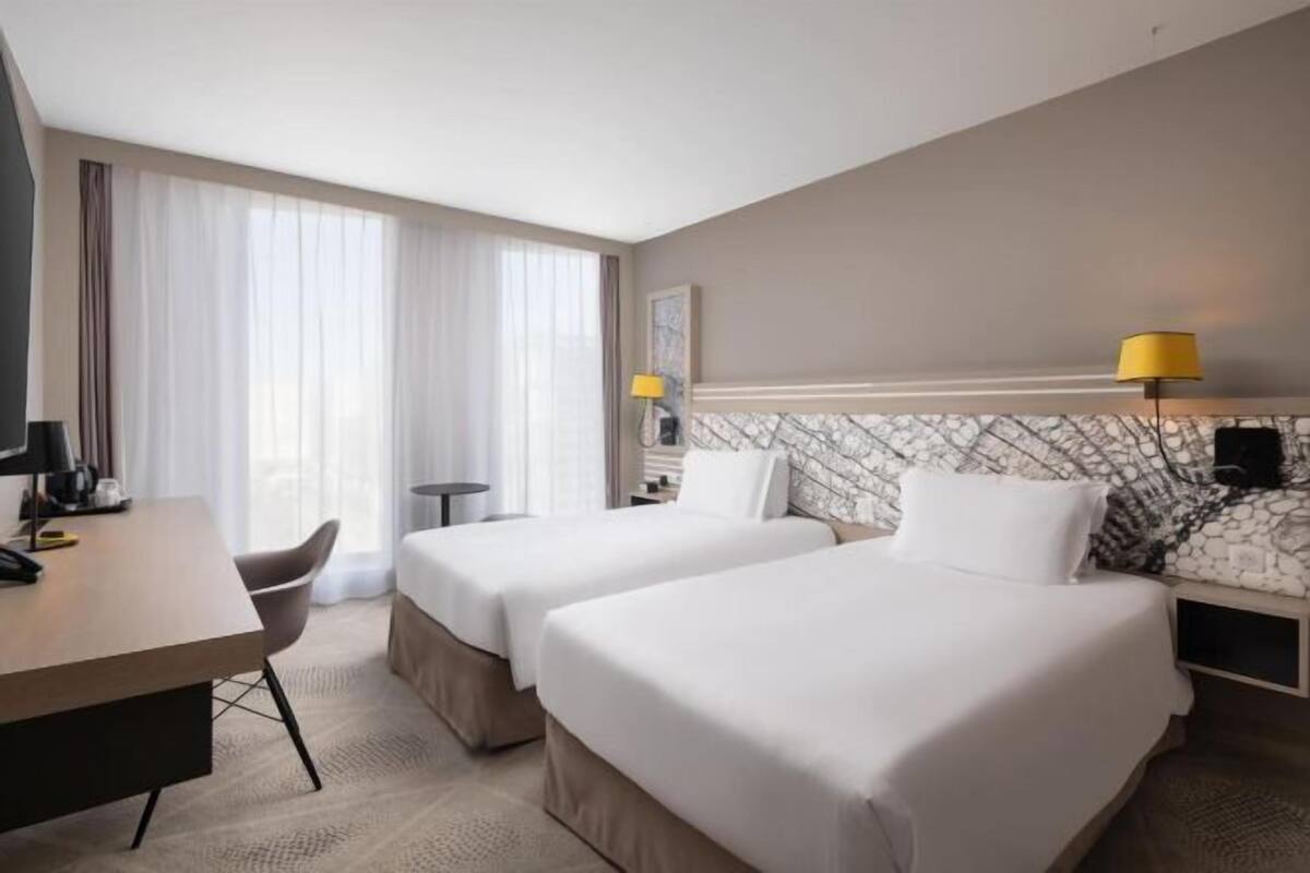 A hotel room with two beds, a desk, a chair, a lamp, and a marble-patterned headboard.