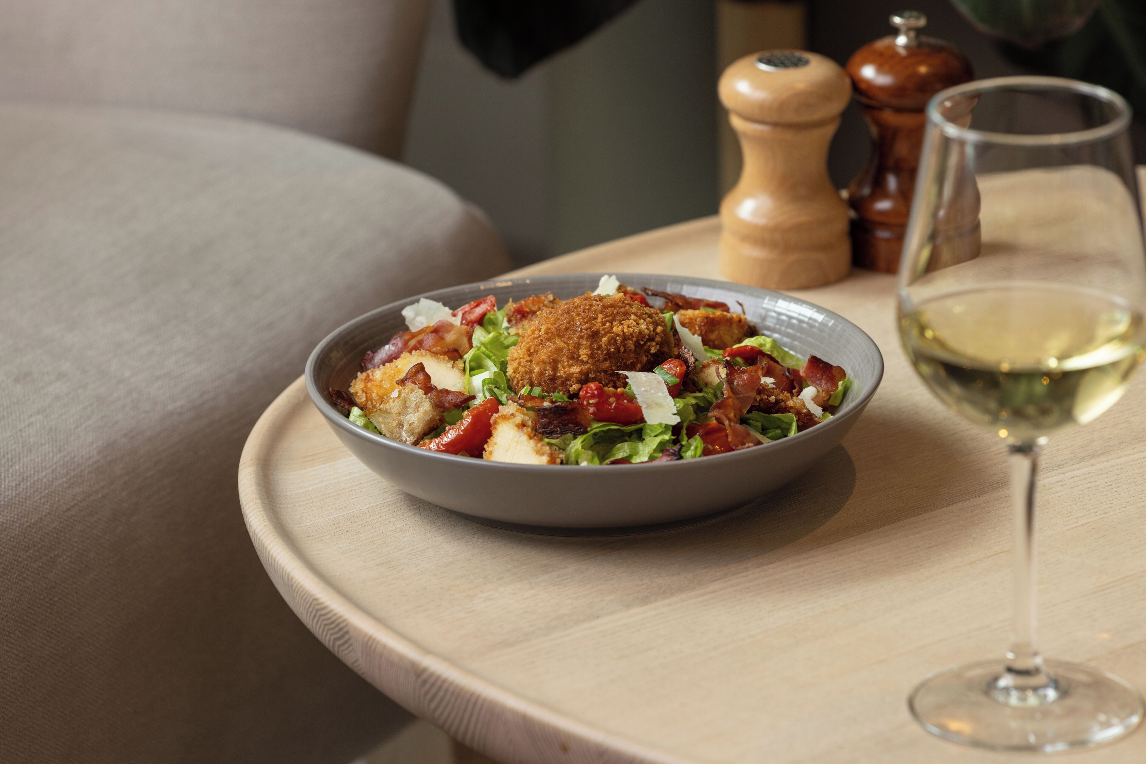 A bowl of salad with croutons and a glass of white wine on a wooden tray.