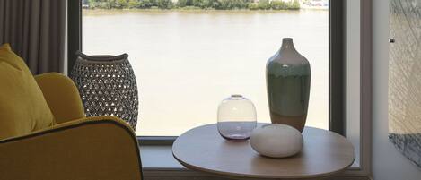 A room with a large window, a yellow chair, a round table with a vase, and a textured wall.