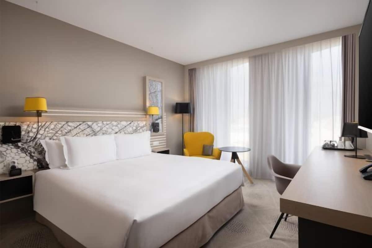 A hotel room with a bed, a desk, a chair, and a small table.