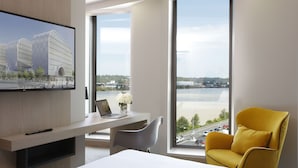 Habitació d'hotel moderna amb una finestra gran, televisió de pantalla plana, escriptori amb un ordinador portàtil, una butaca groga i un llit.