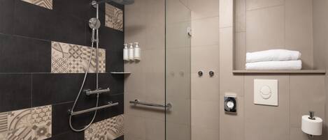 Un baño moderno con mampara de cristal, baldosas estampadas, un perchero y un dispensador de papel higiénico.