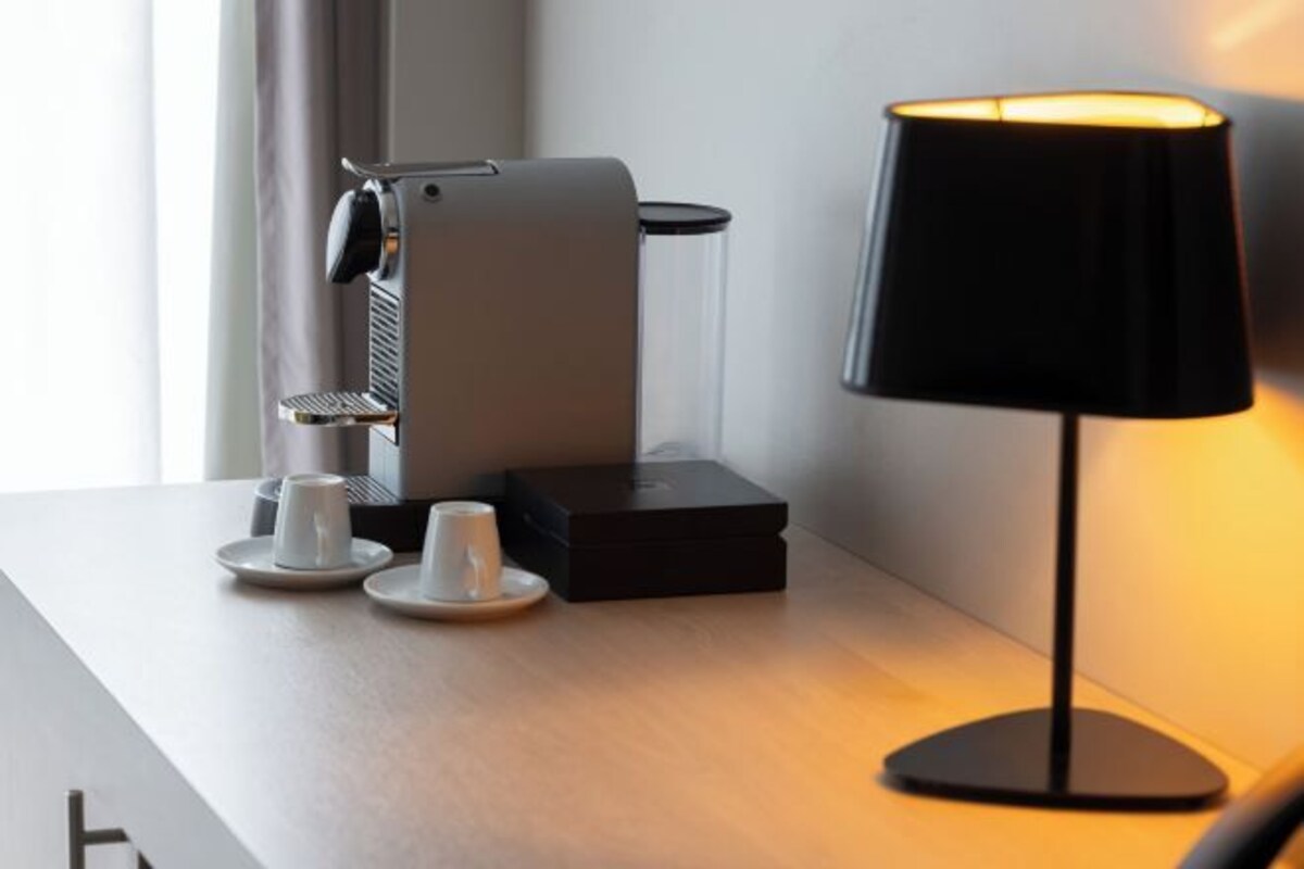 Een koffieapparaat, twee kopjes en een lamp op een tafel.