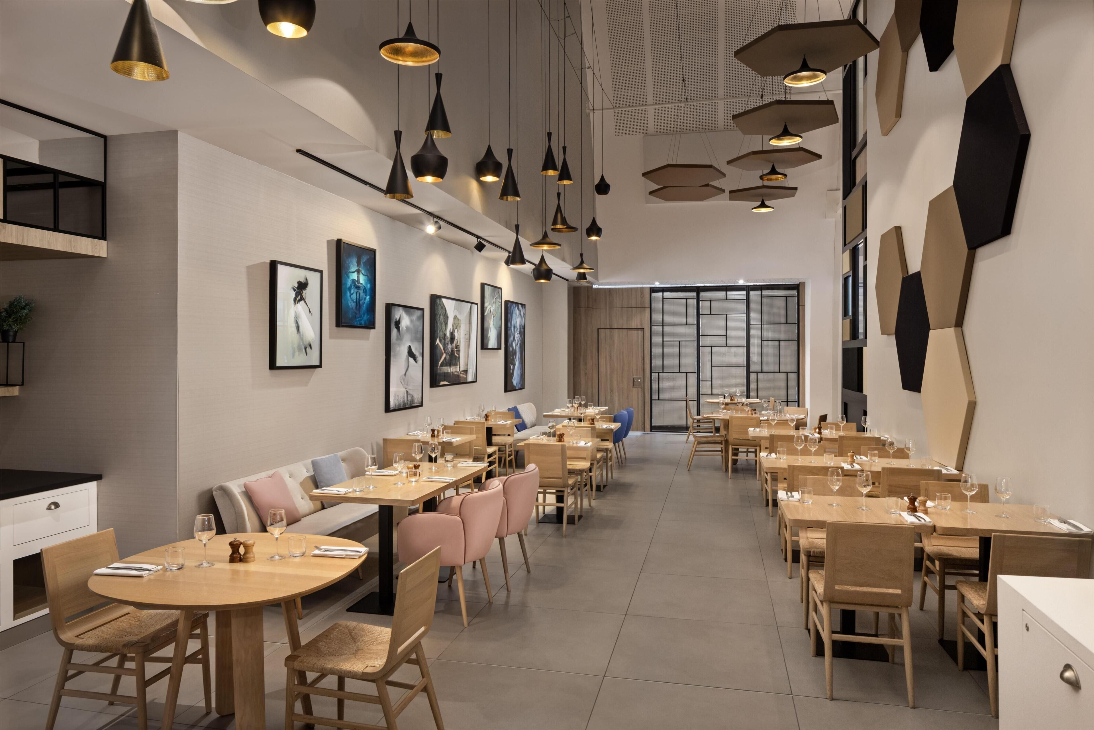 A modern restaurant interior with multiple dining tables and chairs, pendant lighting, and artwork on the walls.