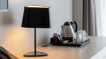 A hotel room with a desk lamp, a coffee maker, and a tray with cups and condiments.