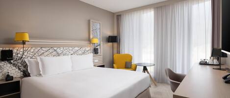 A hotel room with a large bed, a desk, a chair, a small table, and a TV.