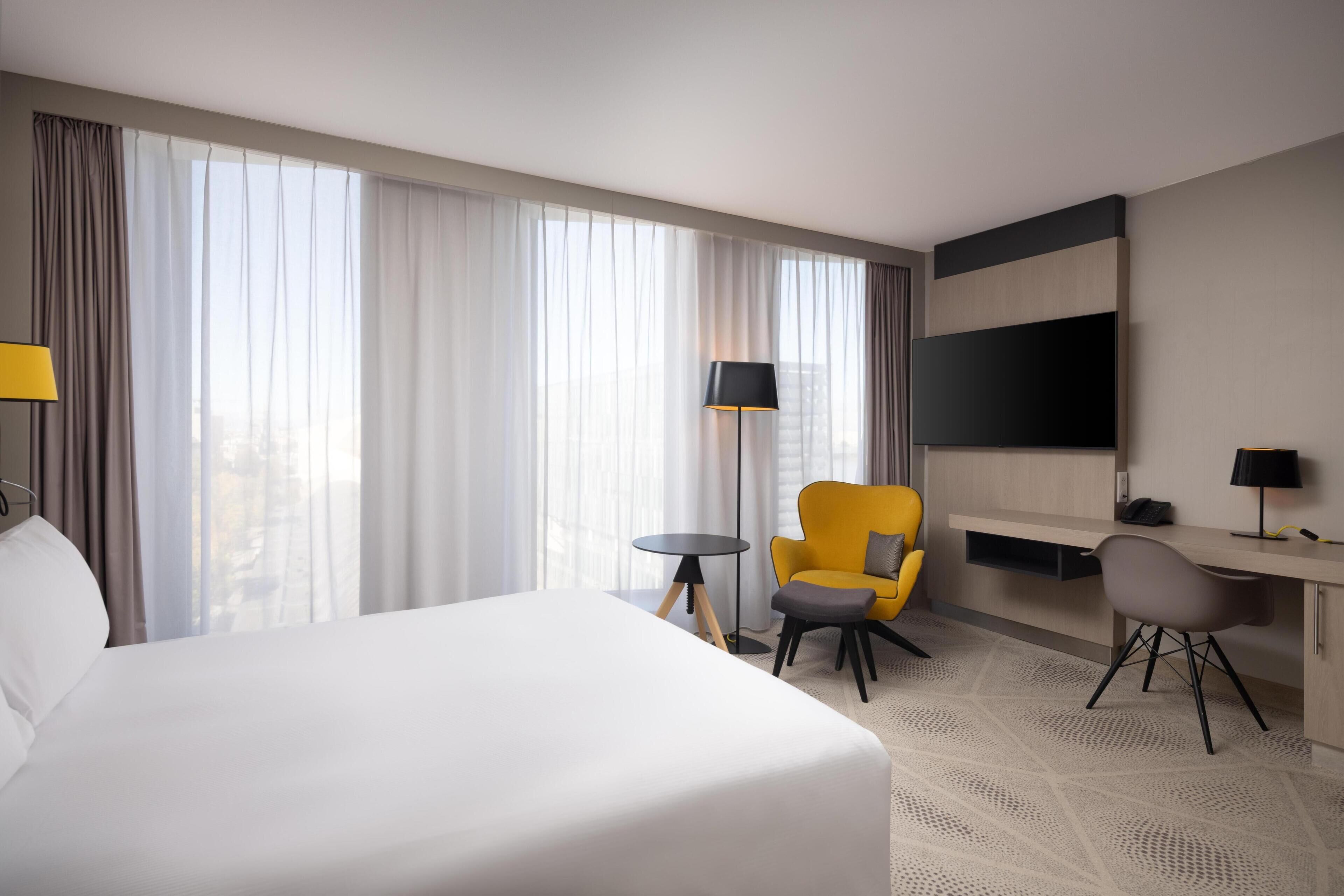 Une chambre d’hôtel avec un grand lit, un bureau avec une chaise, une petite table et un téléviseur fixé au mur.