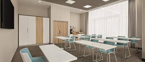 A conference room with white tables and blue chairs, a large window with curtains, and a kitchenette in the background.