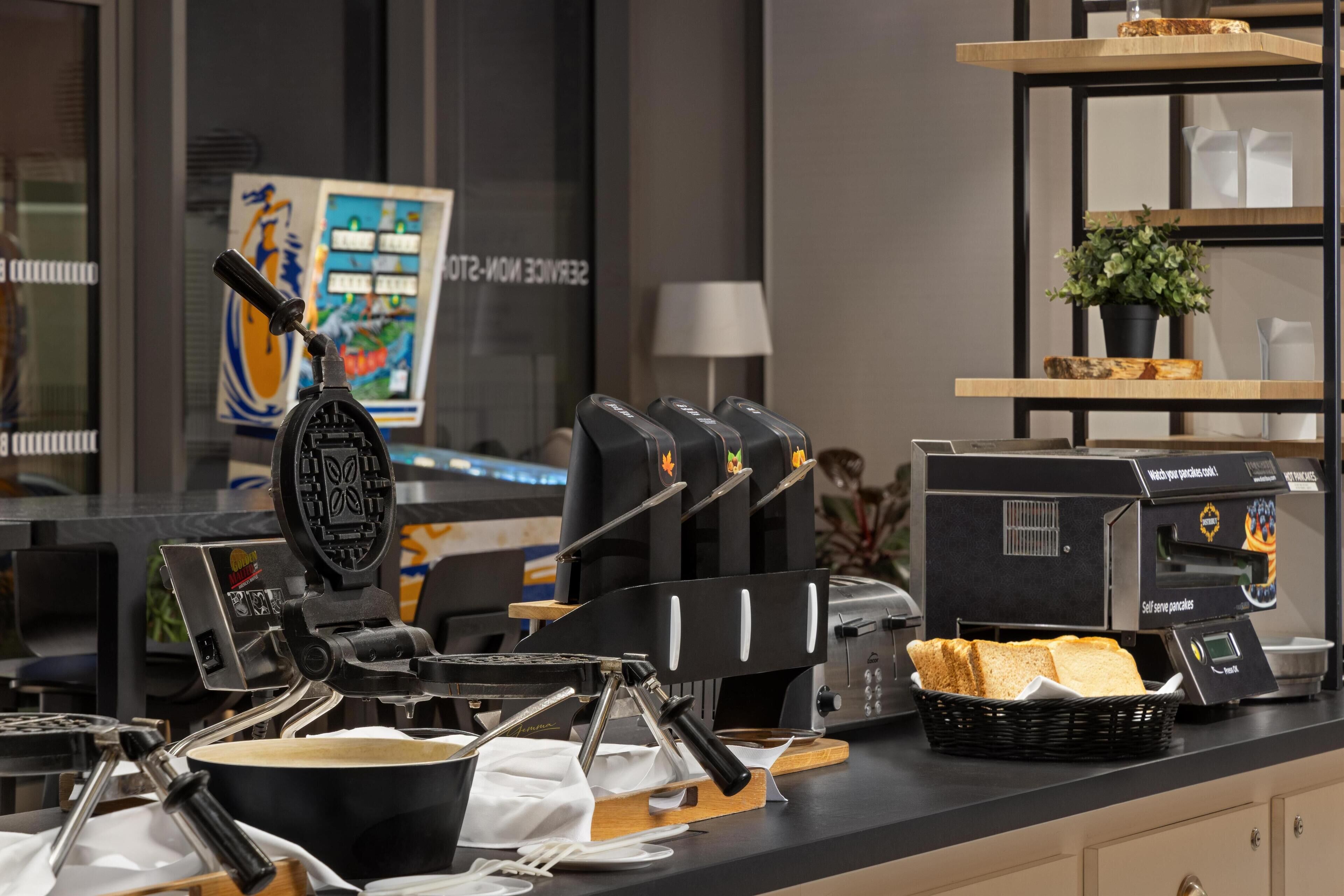 A breakfast bar with a waffle maker, coffee machine, and bread basket.