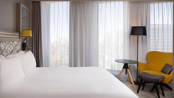 Una habitació d'hotel amb un llit gran, una taula petita, un armari groc i una làmpada de peu.