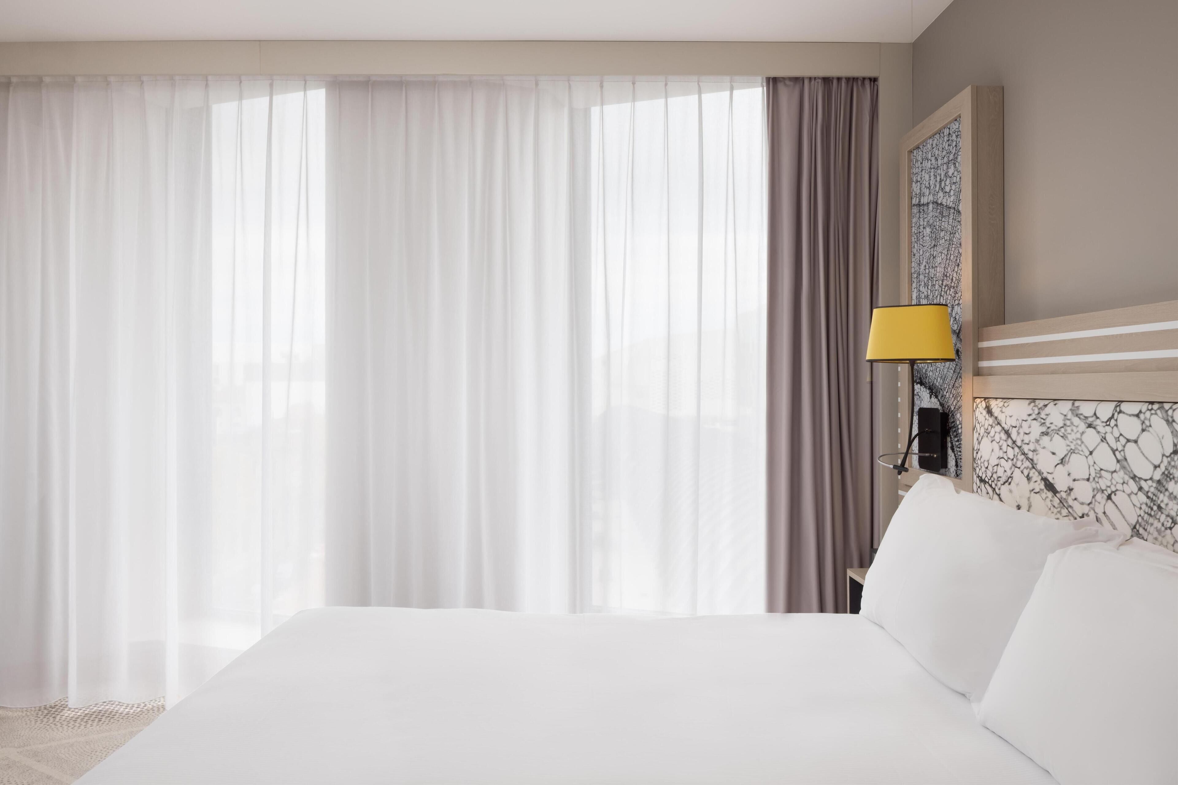 Una habitación de hotel con una cama grande, una mesita de noche, una lámpara y un cuadro en la pared.