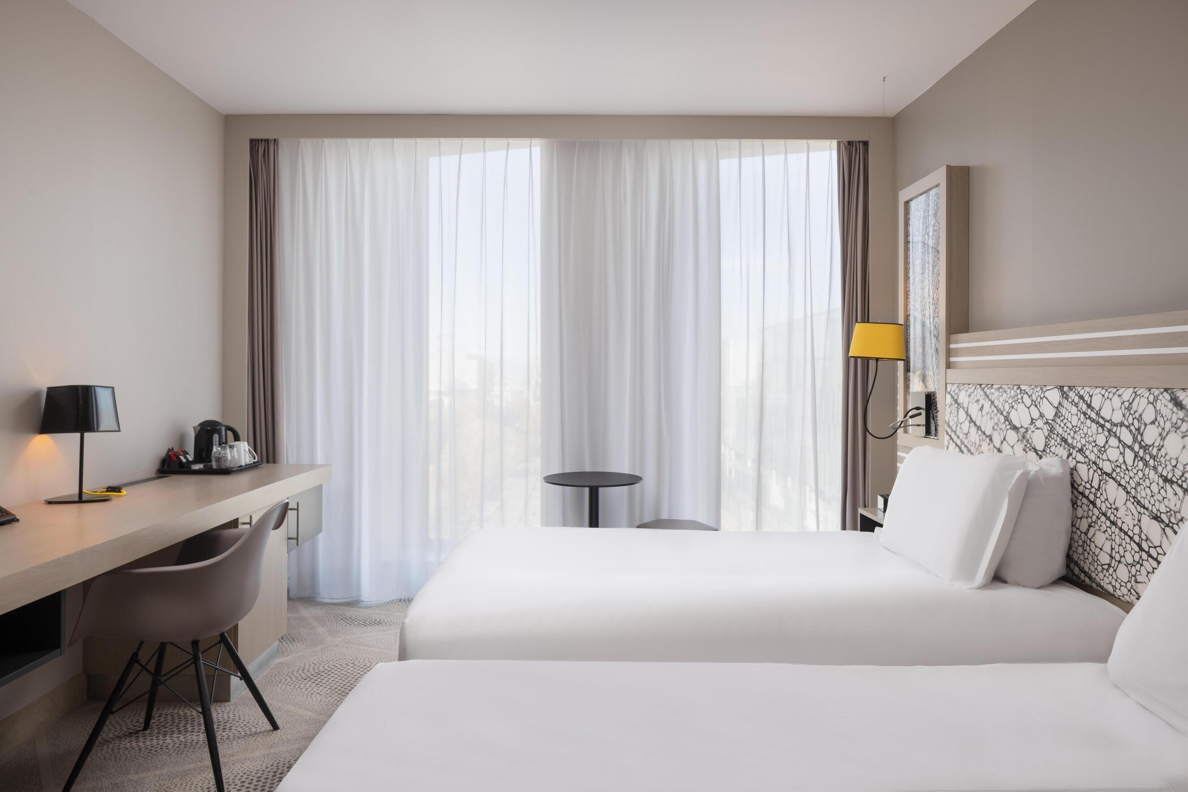 Una habitación de hotel con una cama, un escritorio, una silla, una mesita y una lámpara.