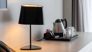 A hotel room with a desk lamp, a coffee maker, and a tray with cups and condiments.