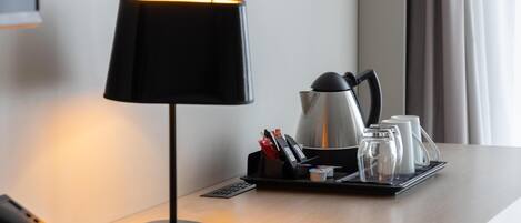 A hotel room with a desk lamp, a coffee maker, and a tray with cups and condiments.