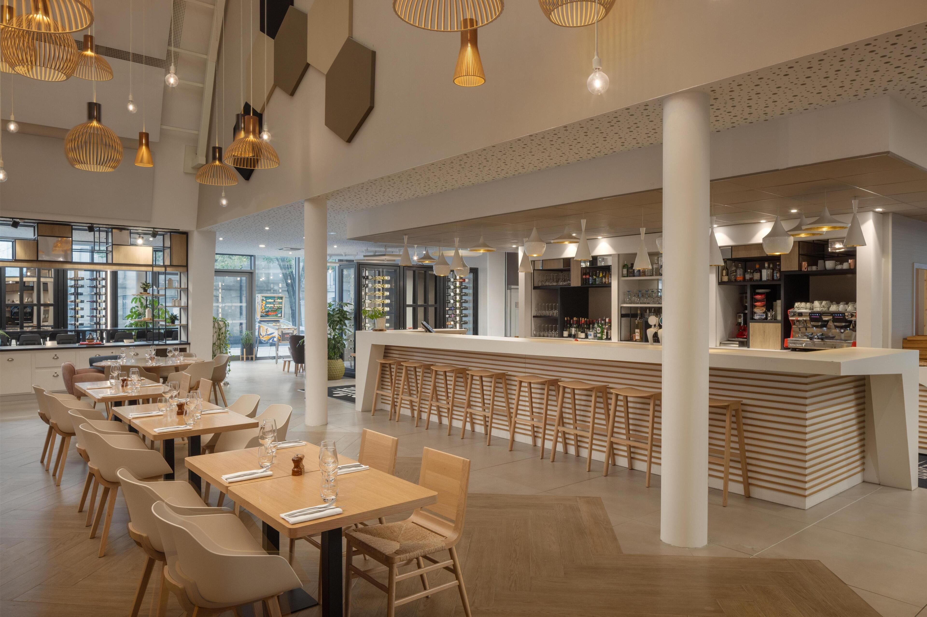 Un restaurante moderno con zona de bar, mesas y sillas de madera, e iluminación colgante.