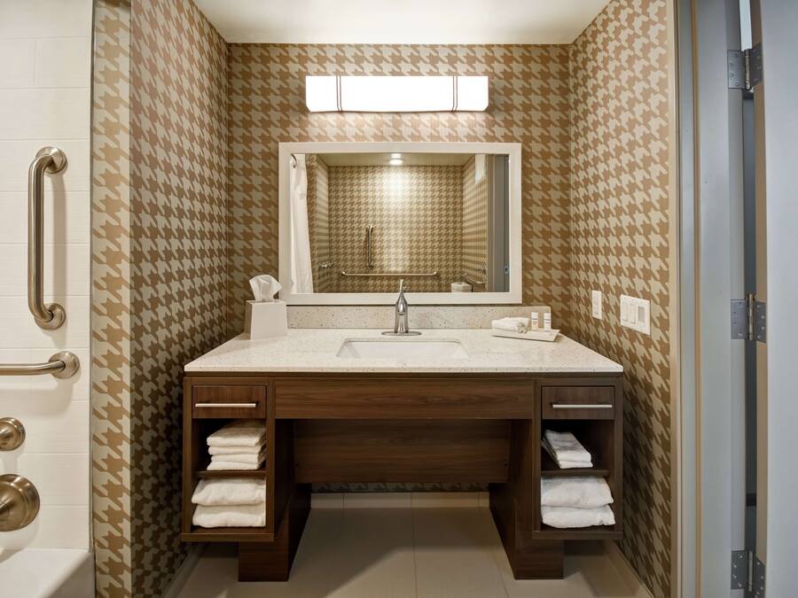 Um banheiro com parede estampada em xadrez houndstooth, uma pia com espelho acima e um porta-toalhas à esquerda.