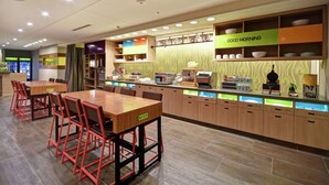 A modern restaurant with a long counter, multiple seating areas, and a variety of dishes displayed on shelves. - Home2 Suites by Hilton Gilbert (Gilbert)