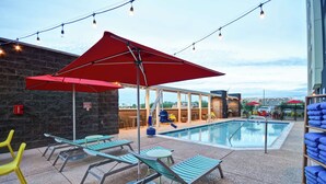 A poolside area with lounge chairs, a red umbrella, and string lights. - Home2 Suites by Hilton Gilbert (Gilbert)