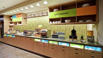 Una barra de desayuno con compartimentos identificados para platos y cubiertos, una máquina de café y un cartel que dice
