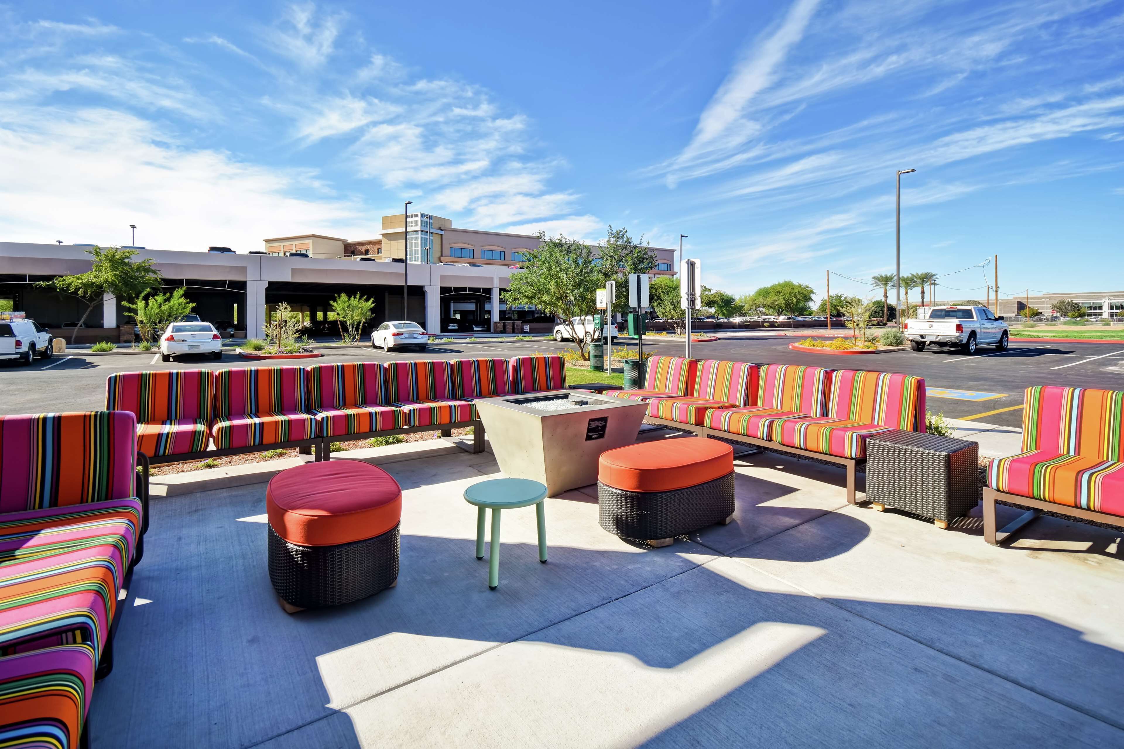 An outdoor seating area with colorful striped sofas and ottomans, a fire pit, and a view of a parking garage and building in the background.