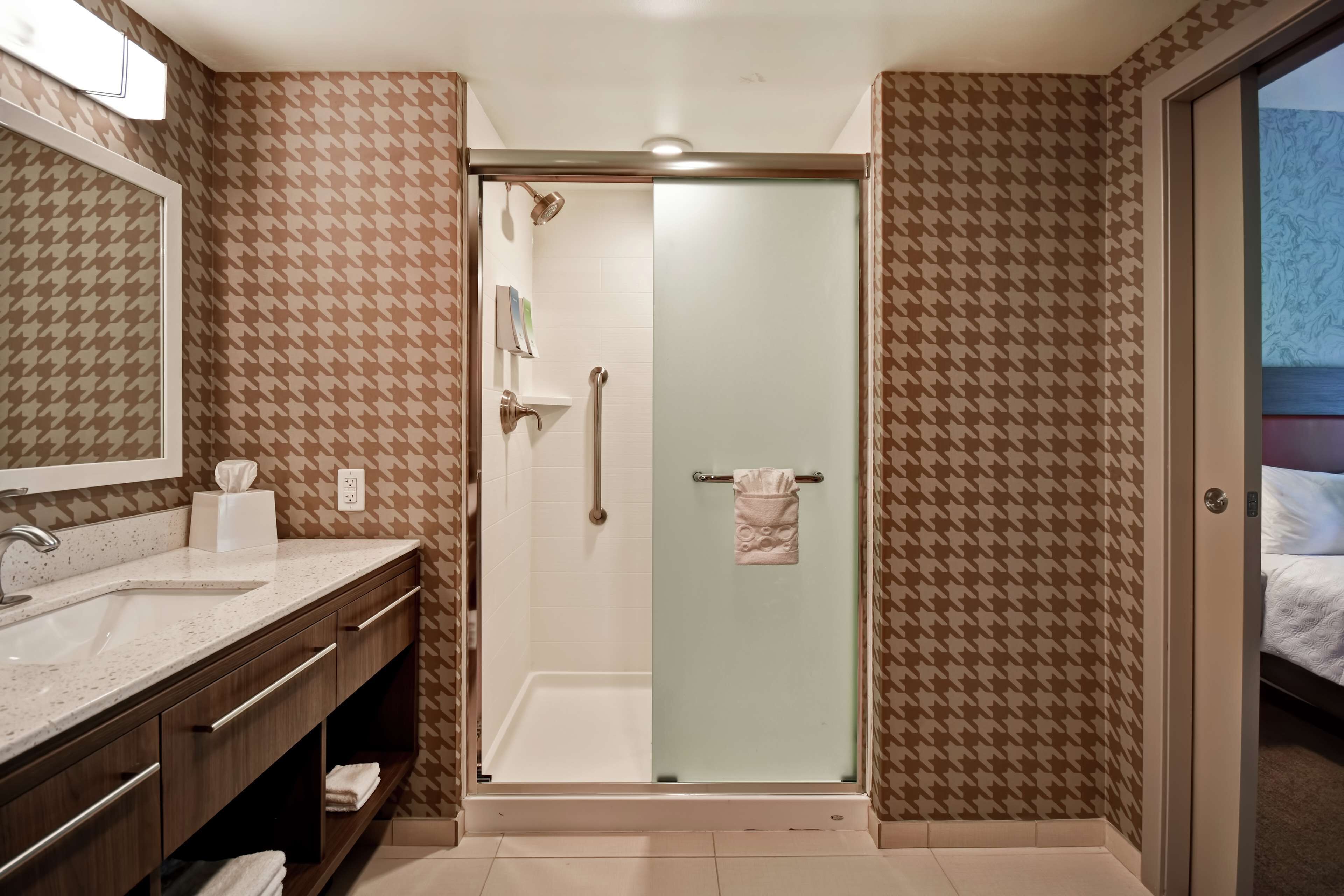A bathroom with a shower, a sink, a mirror, and a towel rack.