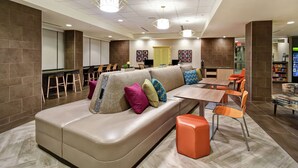 A modern lounge area with a sofa, chairs, a table, and a bar. - Home2 Suites by Hilton Gilbert (Gilbert)