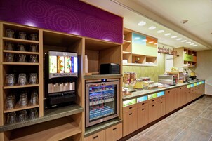 Una estación de bebidas de autoservicio con un refrigerador y una máquina de café.