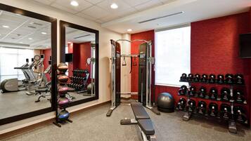 A gym with exercise equipment, a bench, and a wall of dumbbells.